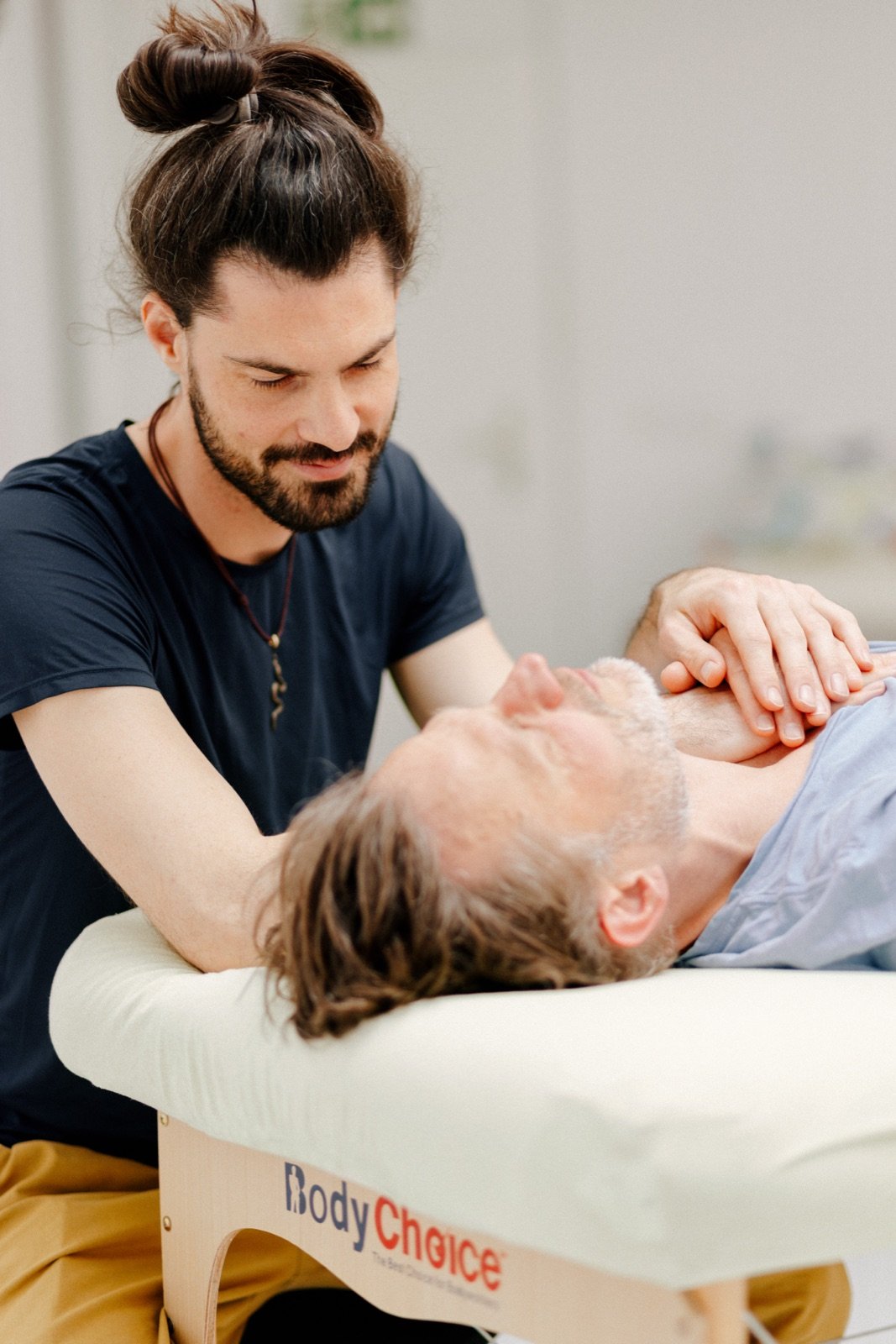 Immanuel leaning in with gentle attention, one hand resting on a client's shoulder during a session
