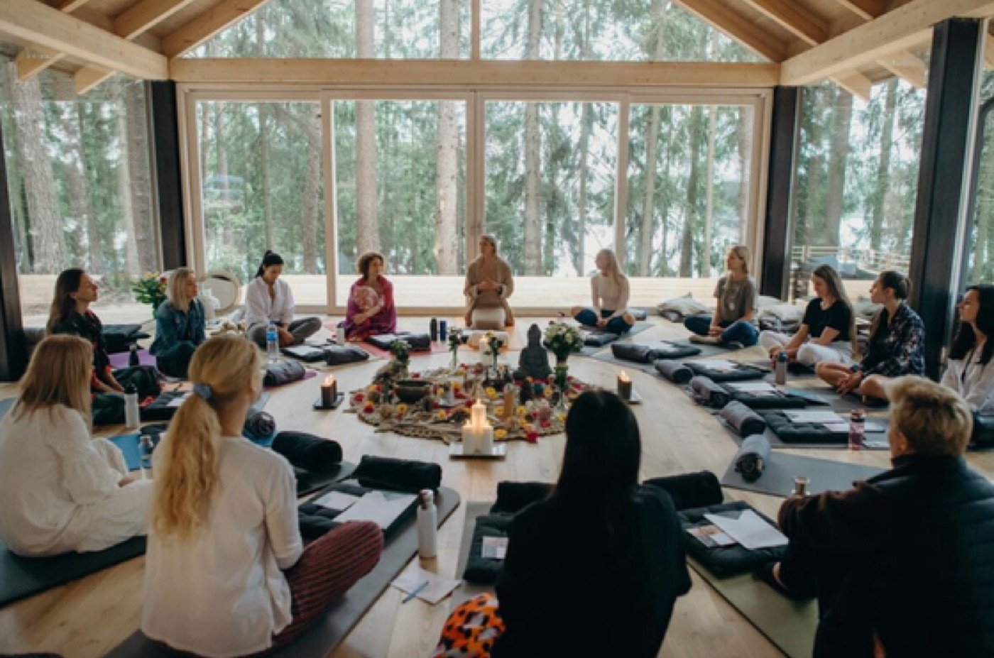 A retreat circle gathered in the glass house, forest visible through the windows